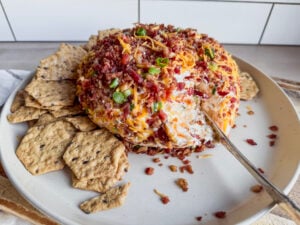 cheese ball with bacon bits on it on a plate with crackers around it