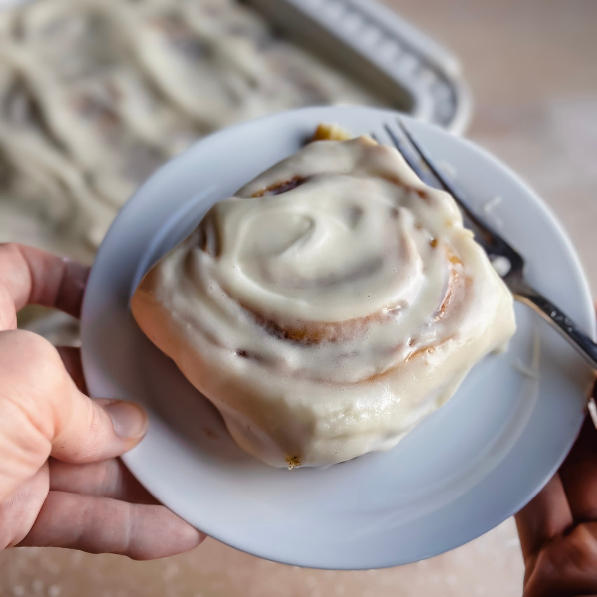 white plate with a gluten free sourdough cinnamon roll on it with a silver fork