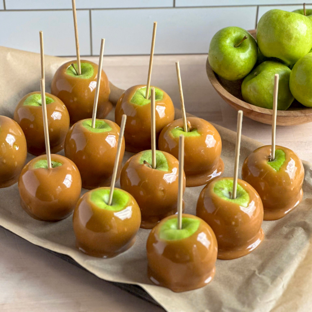 parchment paper lined tray filled with green apples dipped in rich caramel sauce