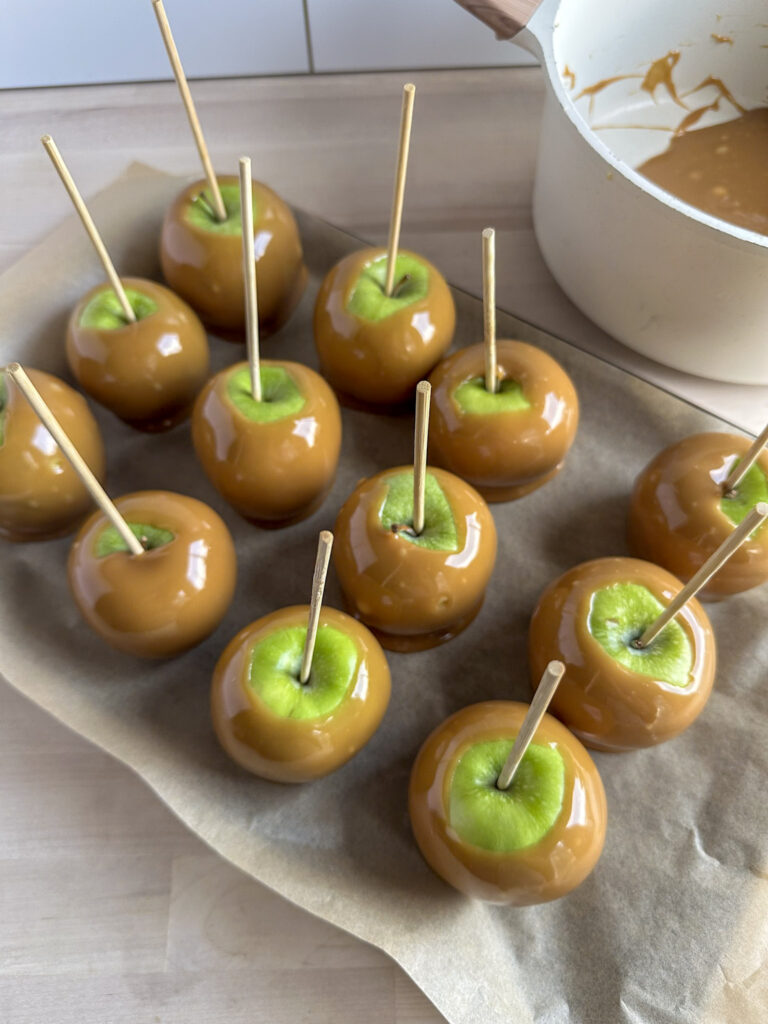 parchment paper lined tray with dipped caramel apples on a stick 