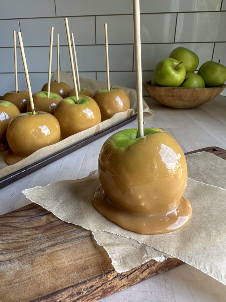 homemade green apples turned into caramel apples on a stick sitting on parchment paper