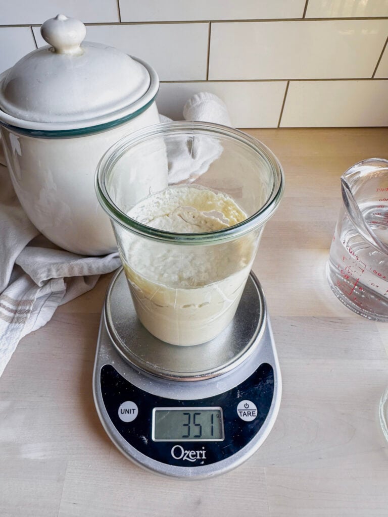 glass jar sits on kitchen scale showing how heavy the starter is