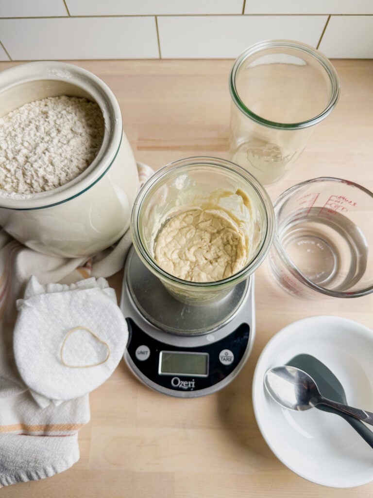 jar of starter on a kitchen scale, brown rice flour in a container near by and water