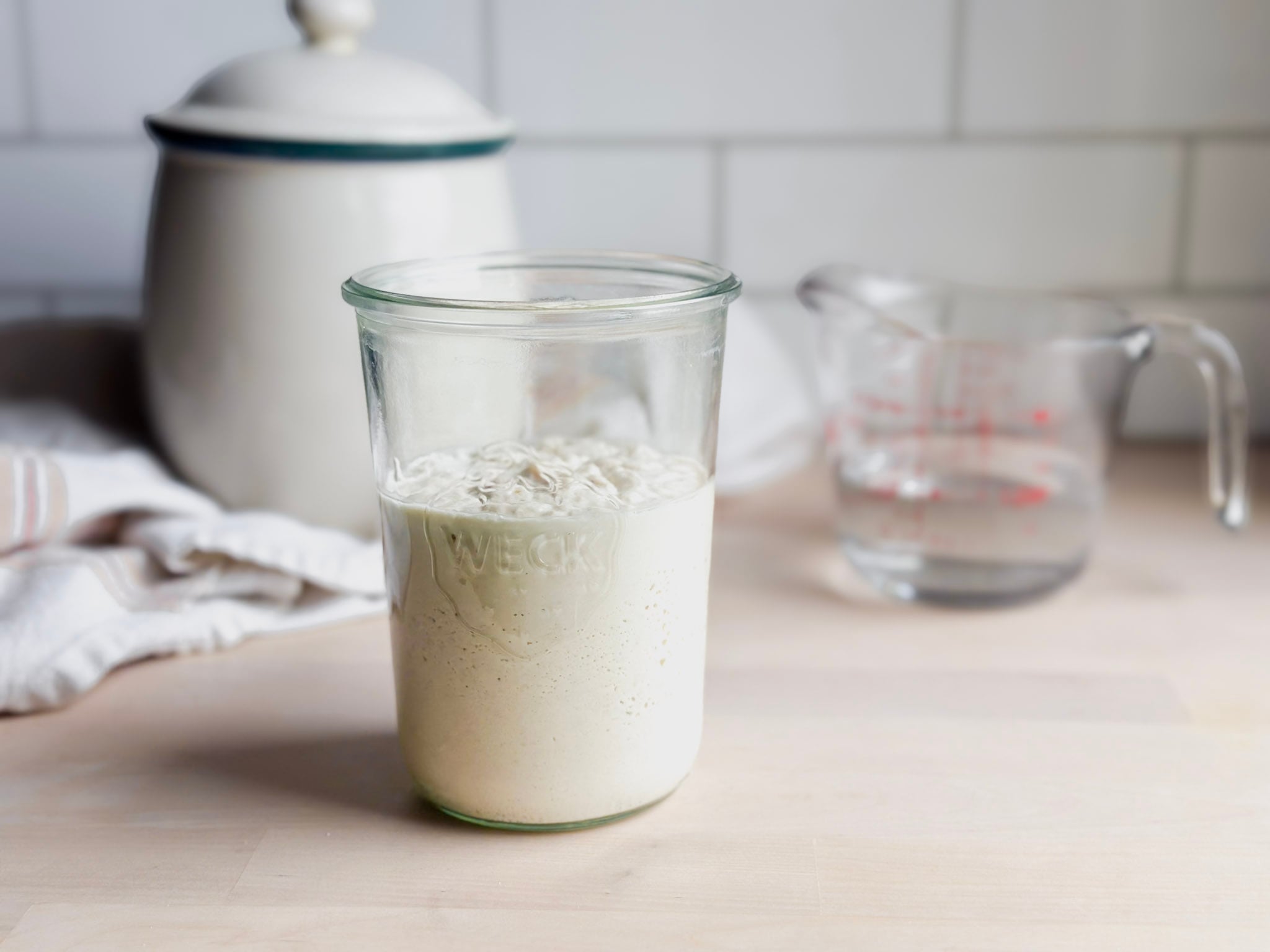 jar of gluten free sourdough on counter with brown rice flour and water near by