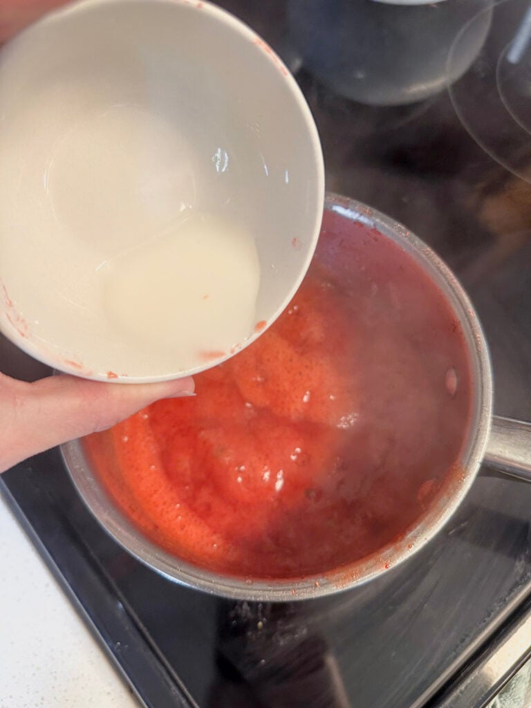 Pouring cornstarch mixture into simmering strawberry syrup