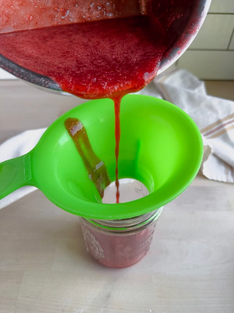pouring strawberry syrup into a glass mason jar