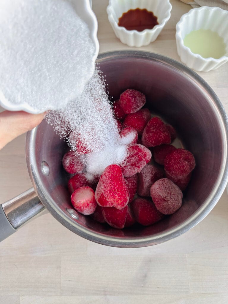 pouring white sugar onto the frozen strawberries
