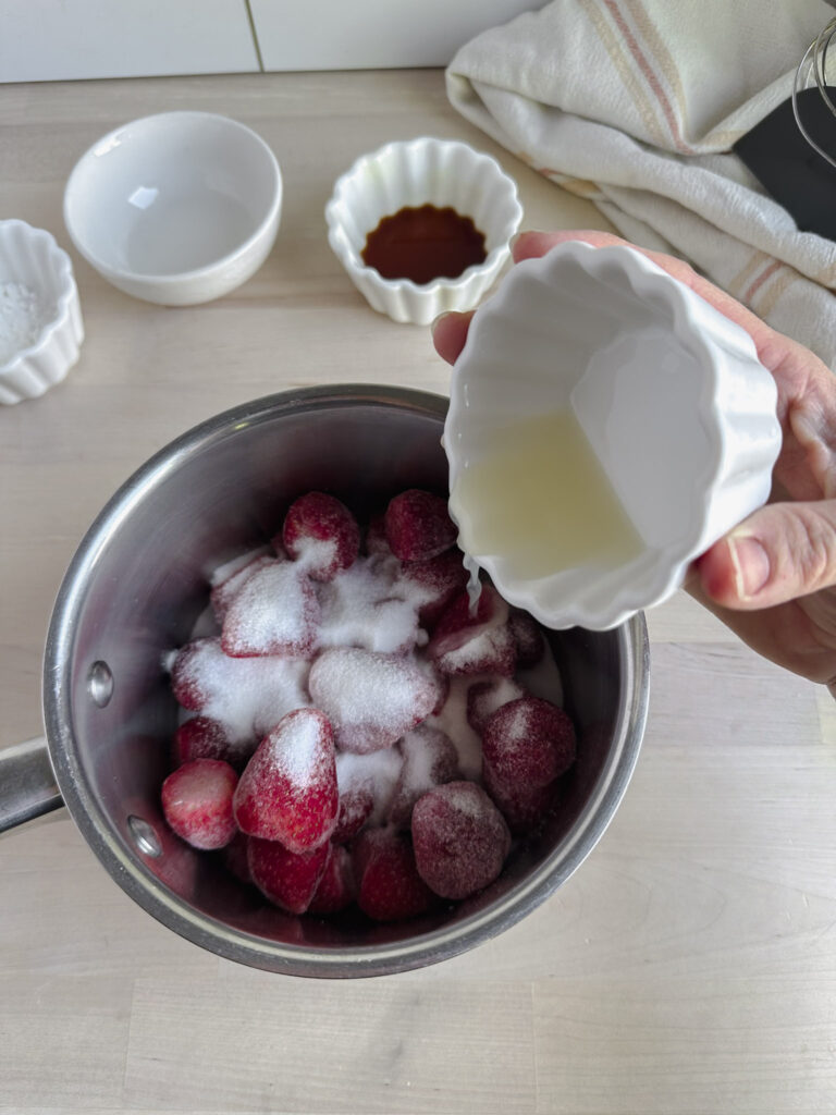frozen strawberries in saucepan with sugar and adding lemon juice to the pot