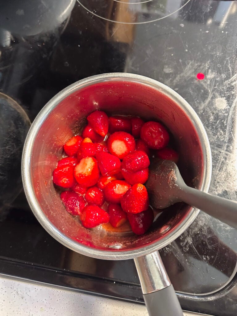 strawberries in sauce pan being stirred to incorporate ingredients