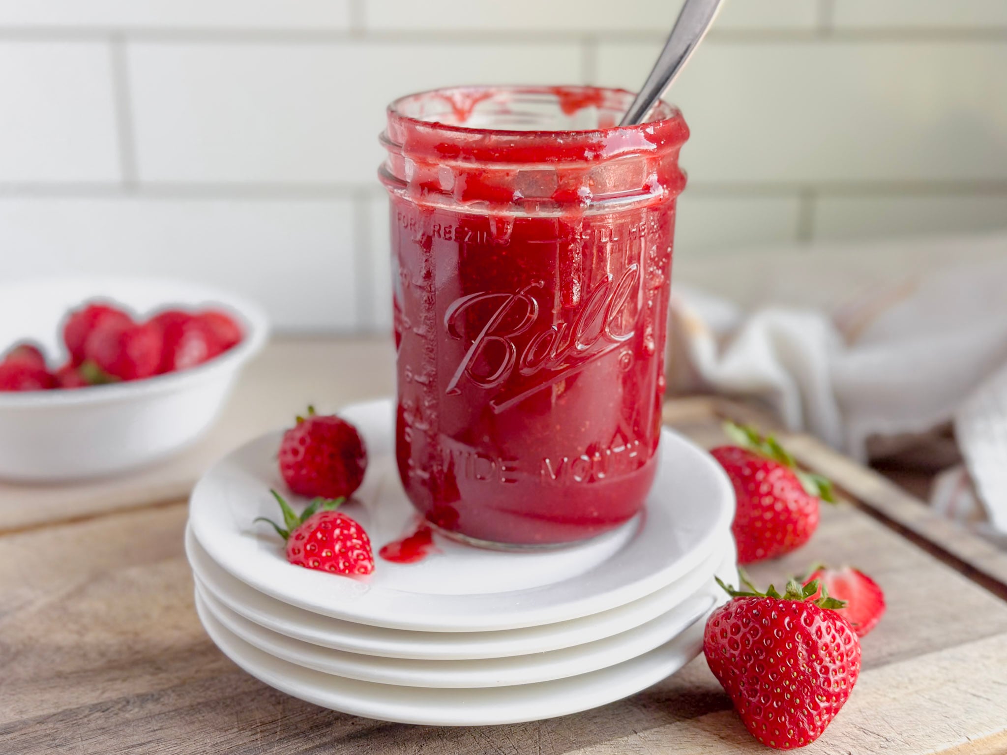 a glass jar filled with strawberry syrup with berries near by