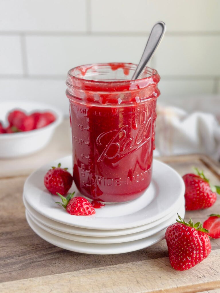 jar of homemade strawberry syrup on stack of white plates
