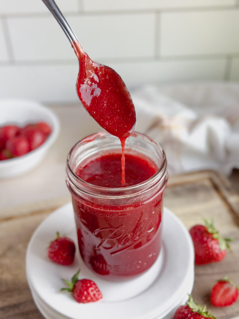 jar of homemade strawberry sauce with strawberries near by