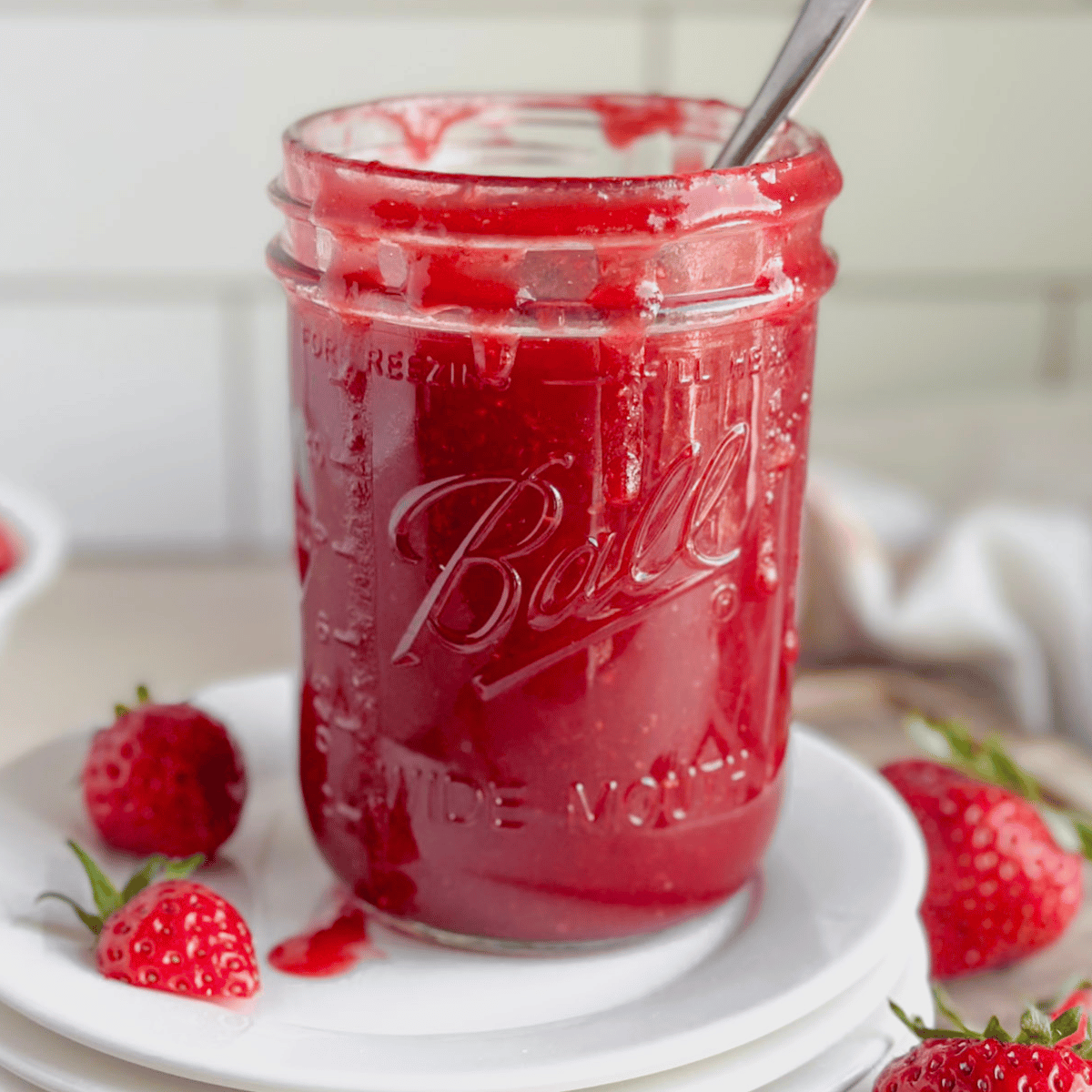 bright red strawberry sauce sitting on plates with strawberries near by
