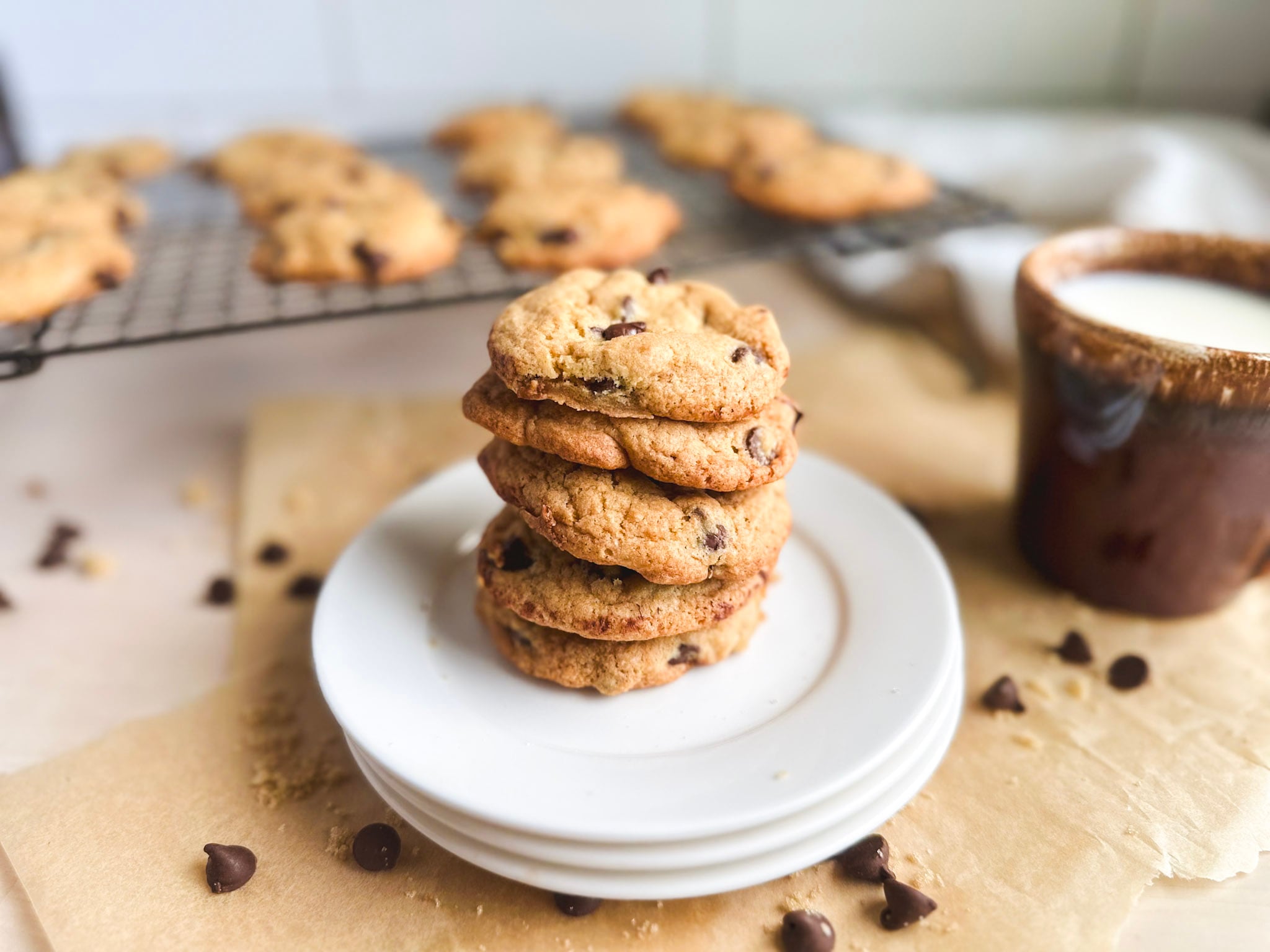 Plate of gluten free sourdough discard chocolate chip cookies stacked tall with a cup of milk near by