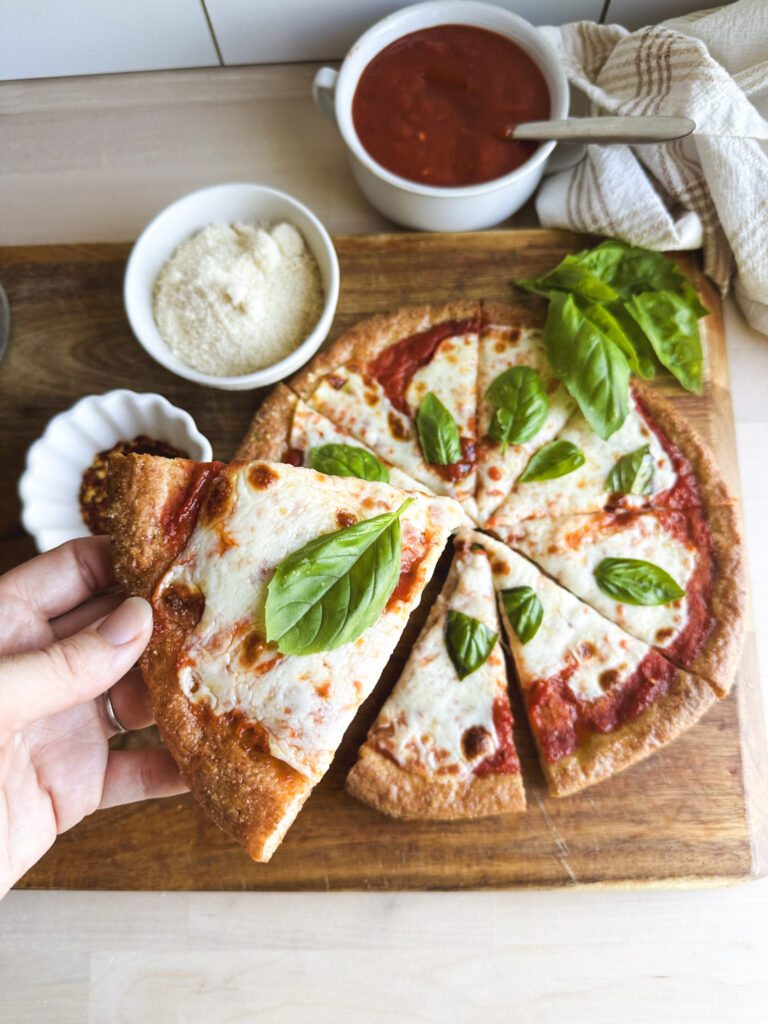 slices of gluten free pizza crust with tomato sauce, pizza sauce, mozzarella and basil leaves
